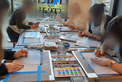 Atelier d’aquarelle avec cinq femmes concentrées en train de peindre dans un magasin de décoration