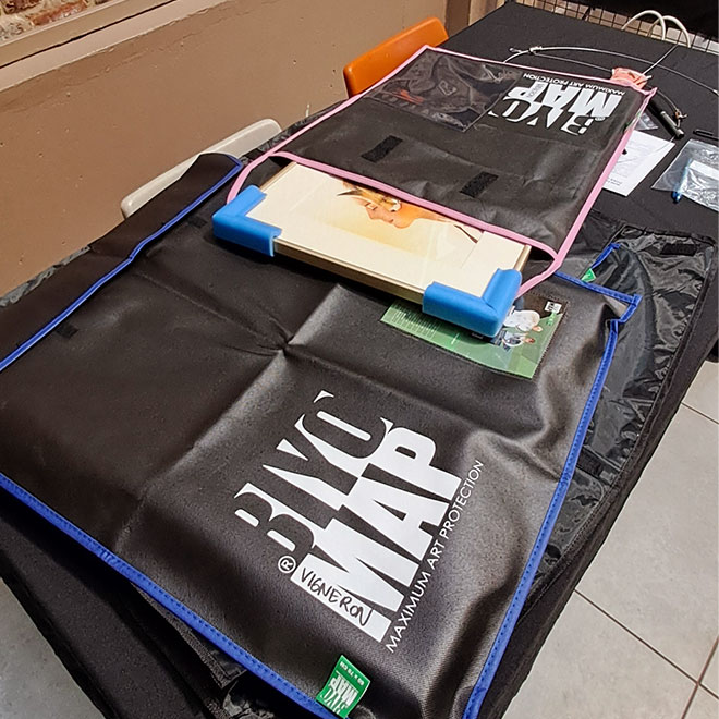 Tableau encadré partiellement sorti d’une pochette de protection réutilisable lors d’un transport pour exposition