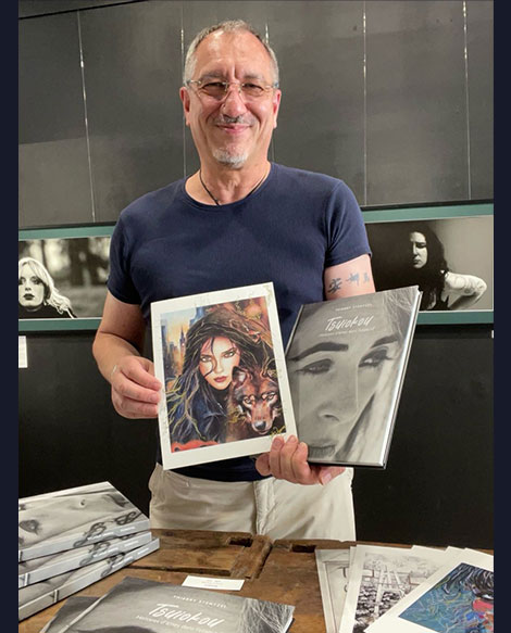 Tierry Stentzel souriant dans sa galerie à Saint-Étienne, tenant le livre Tsuiokou et l’illustration "Julie, la sorcière" rehaussée à la main par Julie Vigneron
